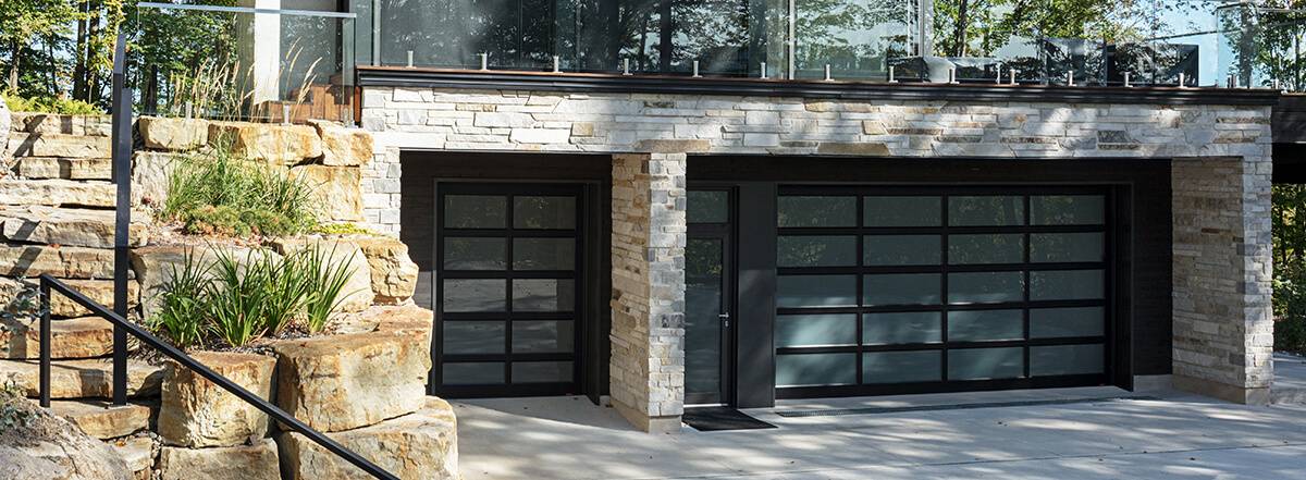 Porte de garage vitrée au complet avec cadre noir modèle California avec des fenêtres satiné sur une maison moderne